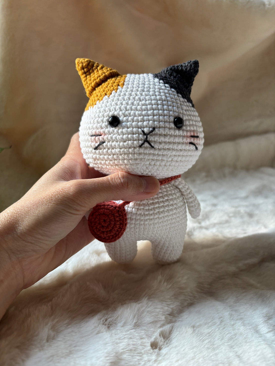Crochet calico cat held in a hand, front view