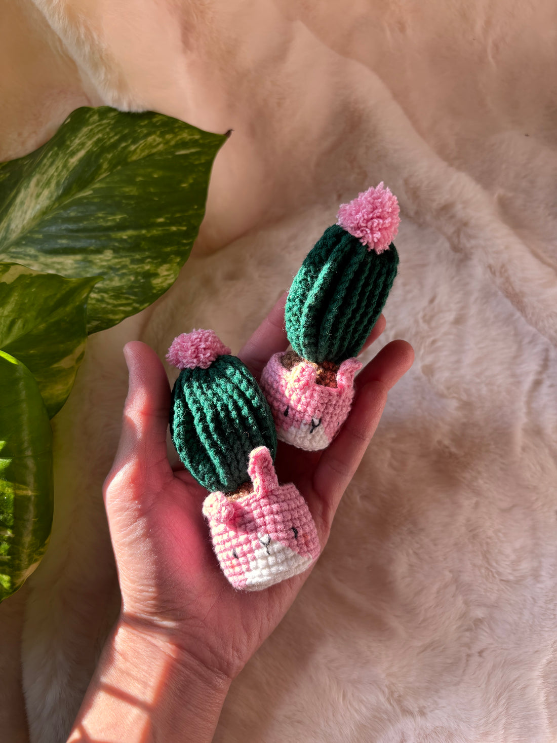 Two crochet cacti in pink bunny pots held in a hand