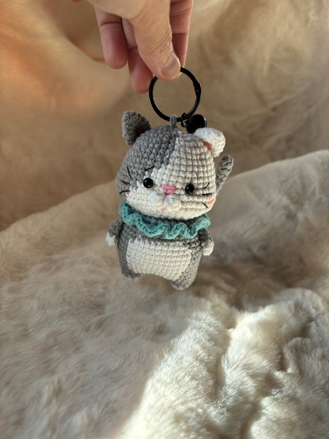 Crochet kitten keychain held by its ring, front view