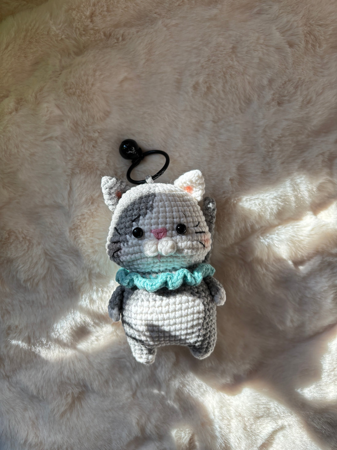 Grey kitten keychain lying on a soft fur rug