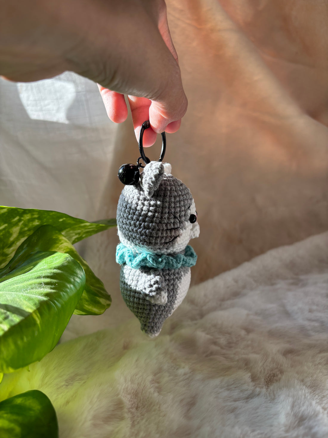 Crochet kitten keychain swinging from a keyring beside leaves