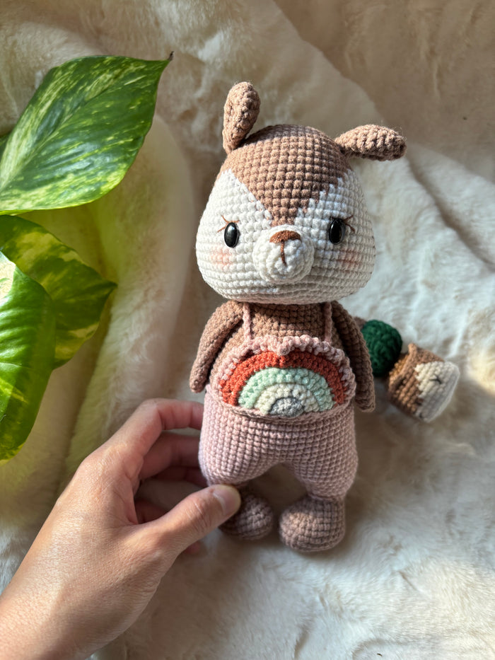 Crochet squirrel in pink rainbow overalls held in a hand