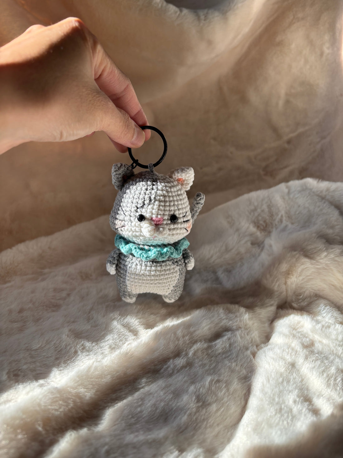 Small crochet kitten keychain held by its ring on a fur rug