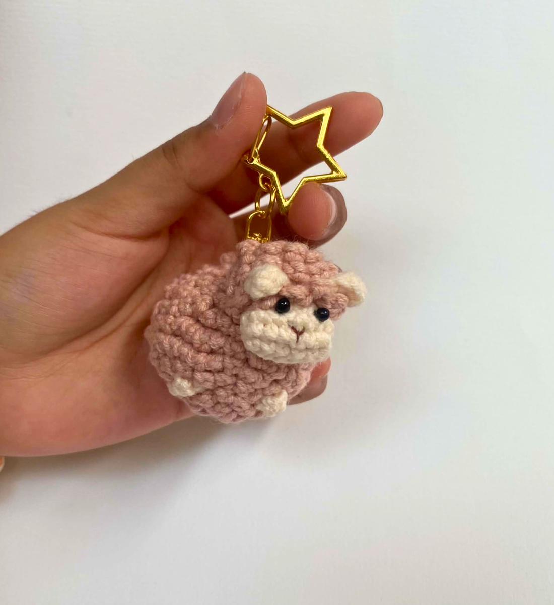 Pink crochet sheep keychain with gold star clasp held in a hand