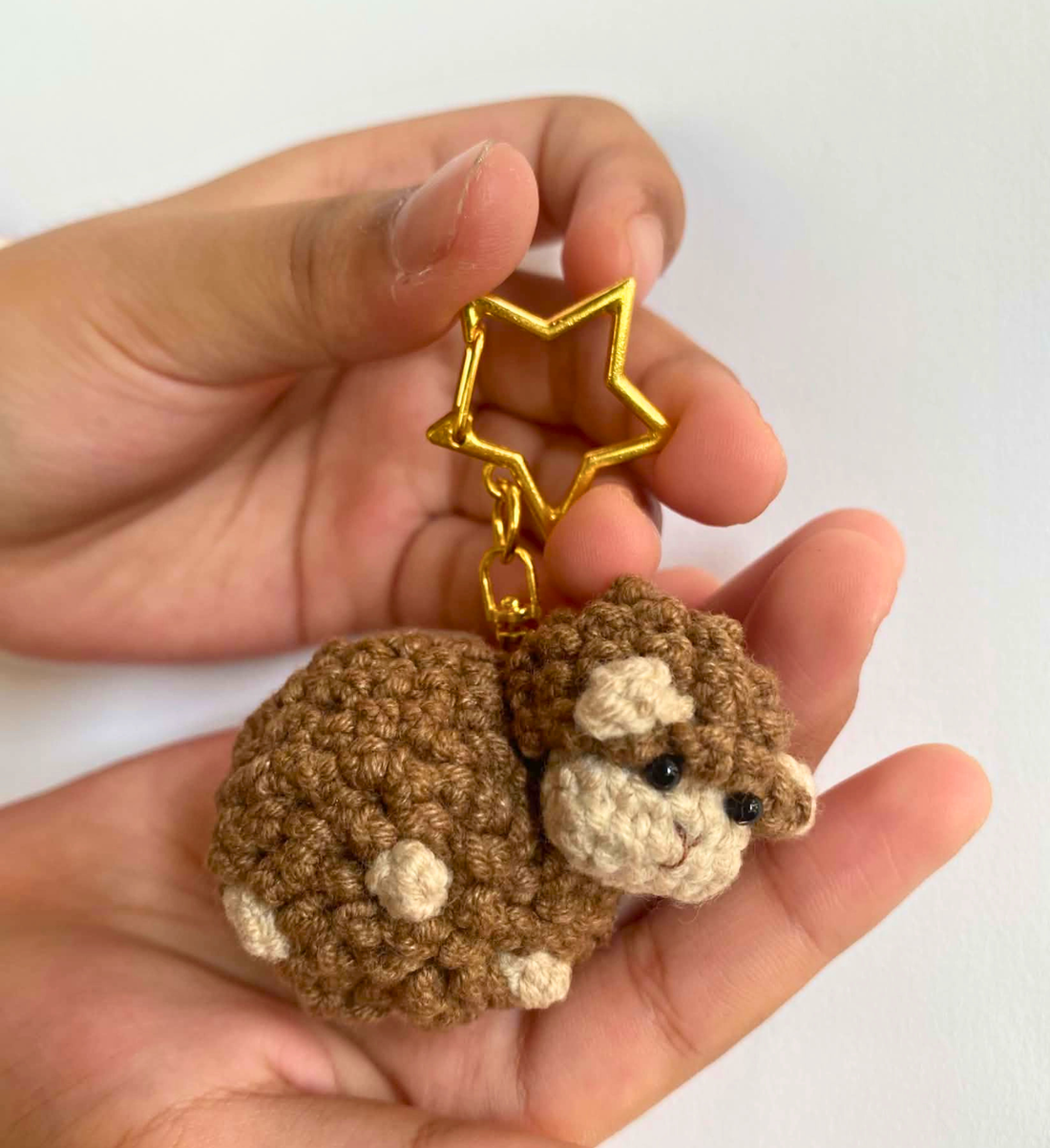 Brown crochet sheep keychain with gold star clasp resting in a hand