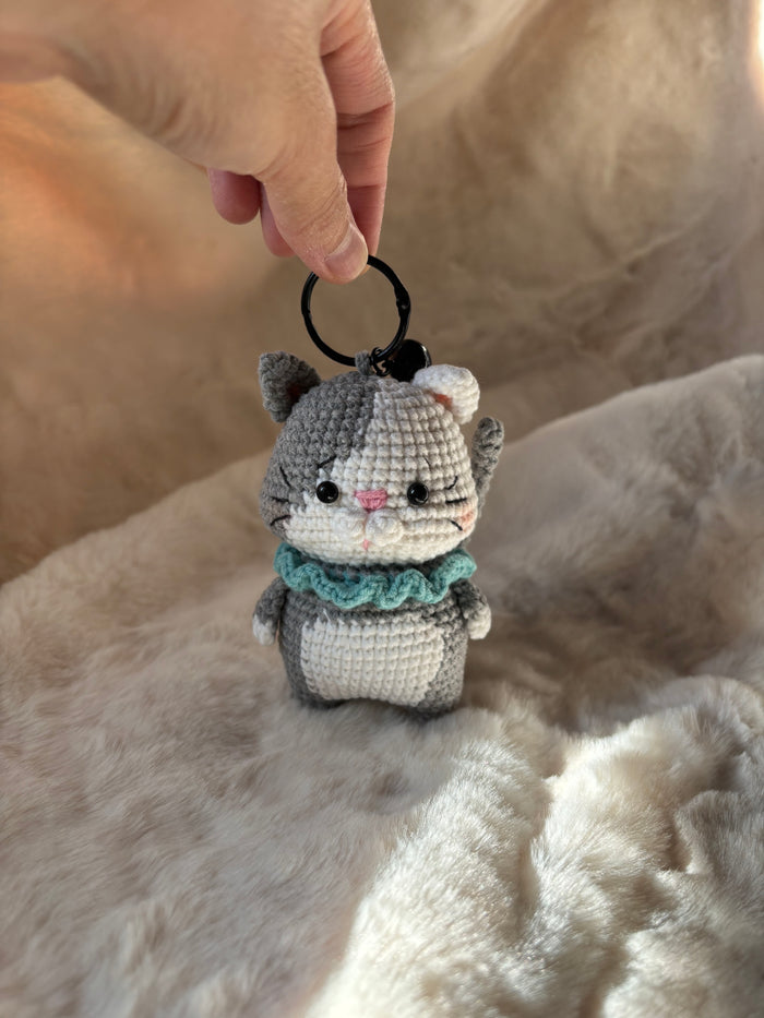 Grey crochet kitten keychain with mint collar hanging from a keyring