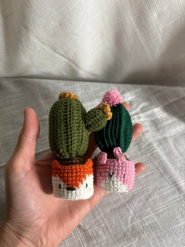 Two small crocheted flowering cacti in fox and bunny pots
