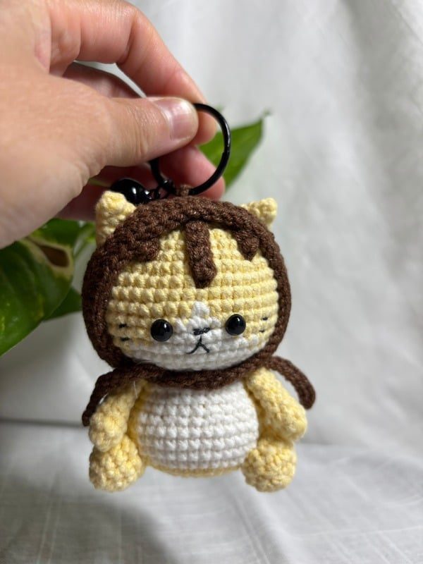 Crocheted yellow kitten keychain in a brown hood