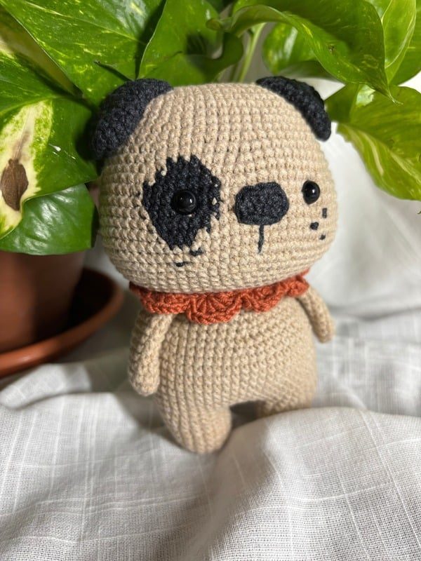 Crocheted beige puppy with an eye patch and orange collar